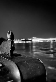 a black and white photo of a boat in the water at night with city lights behind it