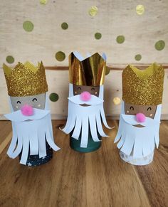 three paper dolls with gold crowns and beards on top of a wooden table next to confetti cones