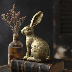 a golden rabbit figurine sitting on top of an old book next to a vase with flowers