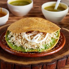 a tortilla filled with shredded chicken and sauces on a wooden tray next to bowls of soup