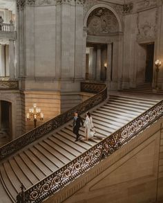 a bride and groom walking down the stairs in an old building with chandeliers