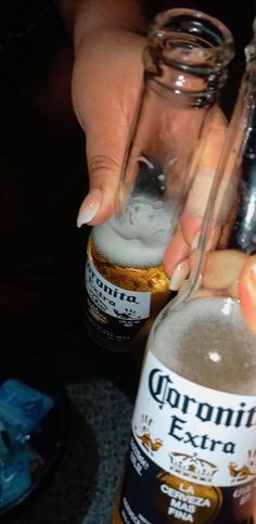 a person is holding two bottles of corona beer