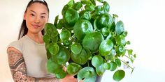 a woman holding up a potted plant with green leaves on it's side