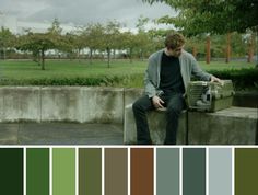 a man sitting on top of a cement wall next to a green park filled with trees