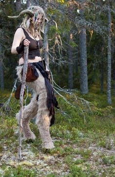 a woman dressed in costume walking through the woods with a dog on her back,