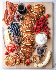 pancakes, strawberries, bananas, blueberries and other foods are arranged on a cutting board