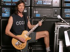 a man sitting on top of a chair holding a guitar in front of a bunch of sound equipment