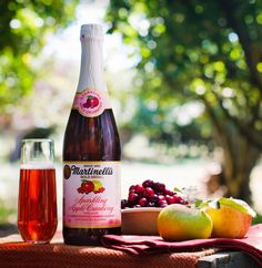 an apple cider, grapes and apples on a table with a bottle of wine