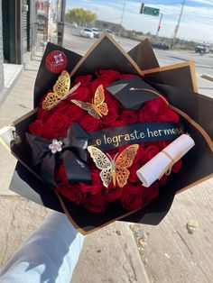 a bouquet of red roses in a black box with gold butterflies and a graduation cap