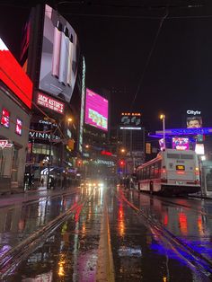 a wet city street at night with traffic lights and billboards on the buildings in the background