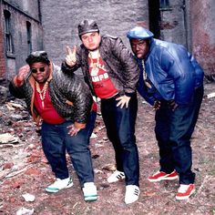 three men standing next to each other in front of a brick building with one man giving the peace sign