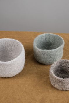 three felt bowls sitting on top of a table next to each other, one gray and one white