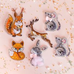 six different animal brooches are shown on a pink surface with gold and white confetti