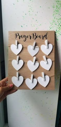 a person holding up a wooden plaque with hearts on it and the words prayer board