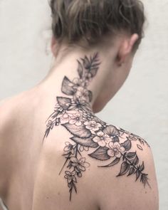 the back of a woman's shoulder with flowers and leaves tattooed on her neck