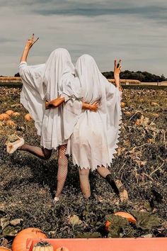 two women dressed as witches in a field with pumpkins on the ground and one holding her head