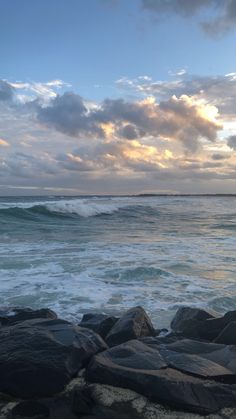 the sun is setting over the ocean and rocks