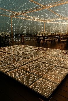 a dance floor covered in lights under a tent with tables and chairs set up for an event