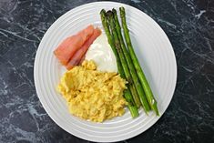 a white plate topped with eggs, asparagus and bacon on top of a black table