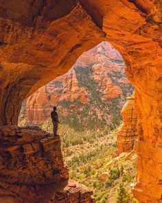 a person standing at the end of a cave in sedona, arizona with mountains in the background