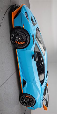 an orange and blue sports car parked on the side of a building with its doors open