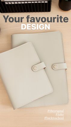 two white leather notebooks sitting on top of a wooden table next to a computer