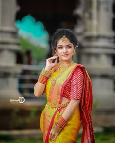 a woman in yellow and red sari posing for the camera with her hand on her ear