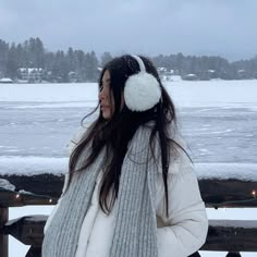 a woman standing in the snow next to a bench with ear muffs on her head