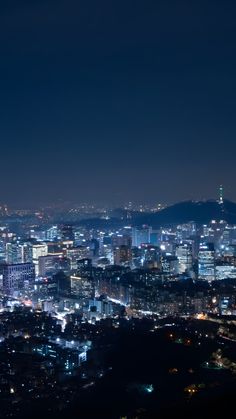 the city is lit up at night with bright lights in the buildings and hills behind it