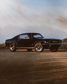 an old black muscle car parked on the side of the road