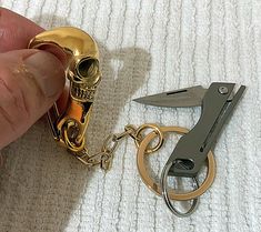 a hand holding a gold colored pocket knife next to a skull shaped keychain