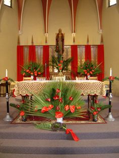 the interior of a church decorated with red flowers and greenery, candles and pews