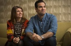 a man and woman sitting on a couch looking at something in the distance with their arms crossed