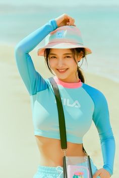 a young woman is standing on the beach wearing a hat and holding a book in her hand