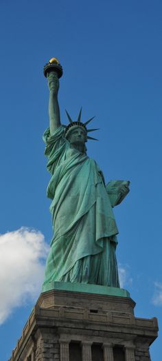 the statue of liberty is shown against a blue sky with clouds in the foreground