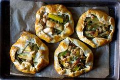 four small pies on a baking sheet with some toppings in the top one