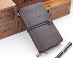 a brown leather journal sitting on top of a table next to two boxes and a pen