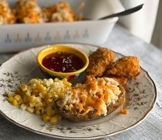 a white plate topped with potatoes and corn next to a bowl of ketchup