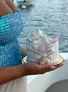 a woman holding a cake with seashells on it