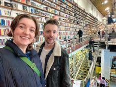 two people standing next to each other in front of a book store filled with books