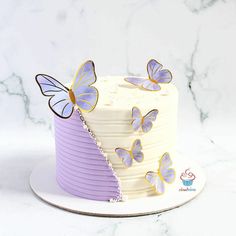 a white cake with purple frosting and butterflies on top, sitting on a plate