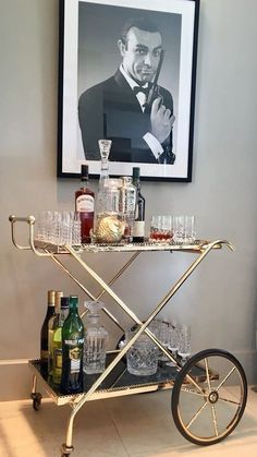 a bar cart with glasses and bottles on it in front of a framed photo above