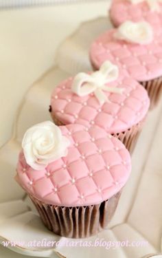 three cupcakes decorated with pink icing and white flowers on a platter