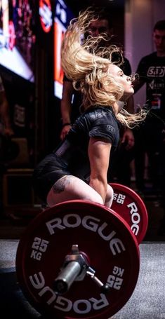 a woman is squatting with a barbell in her hand and she has long blonde hair