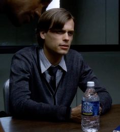 a man sitting at a table in front of a bottle of water