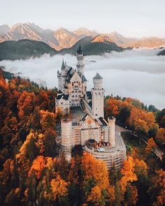 an aerial view of a castle surrounded by trees in the fall with fog and low lying clouds