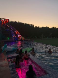 people are sitting in the pool at night, with lights on and inflatable rafts