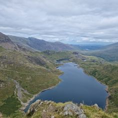 a lake in the middle of some mountains with hills and grass on either side that is surrounded by water