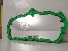 a green mirror sitting on top of a white counter next to a chandelier