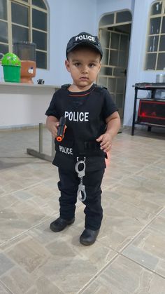 a little boy wearing a police shirt and hat standing in a room with tile flooring